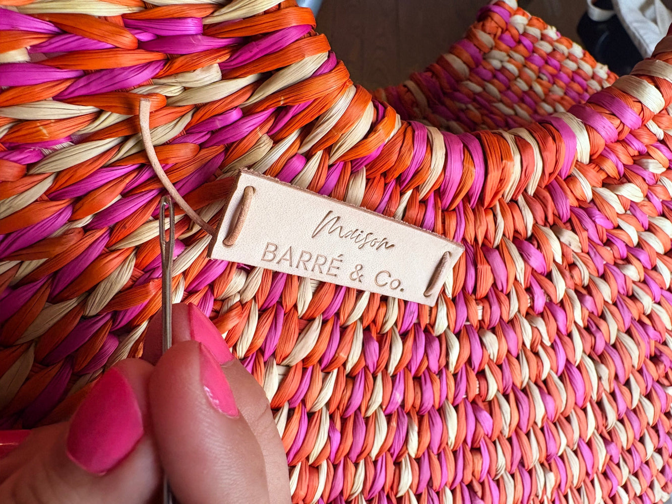 Colorful woven bag with a brand tag being adjusted by a hand holding a needle.